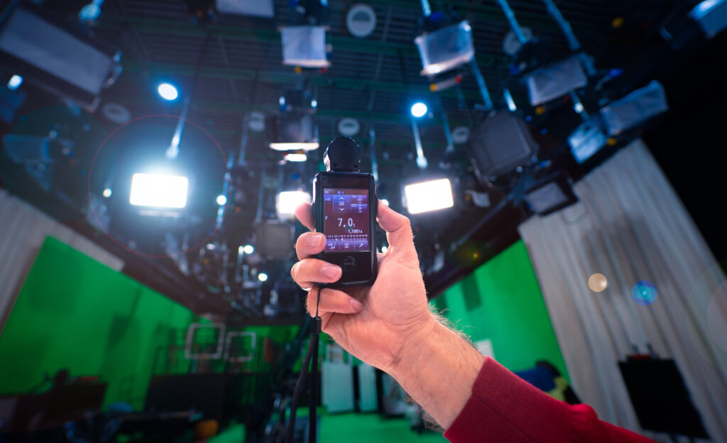 A lighting technician measuring light quality and brightness in TV studio holding a light meter in hand