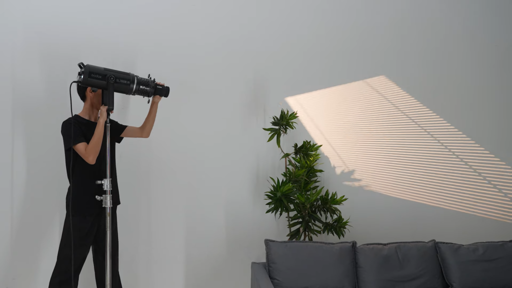 Lighting technician adjusting the angle of window blinds gobo in a studio using Godox BLP Projection Attachment for COB LED Bowens mount lights