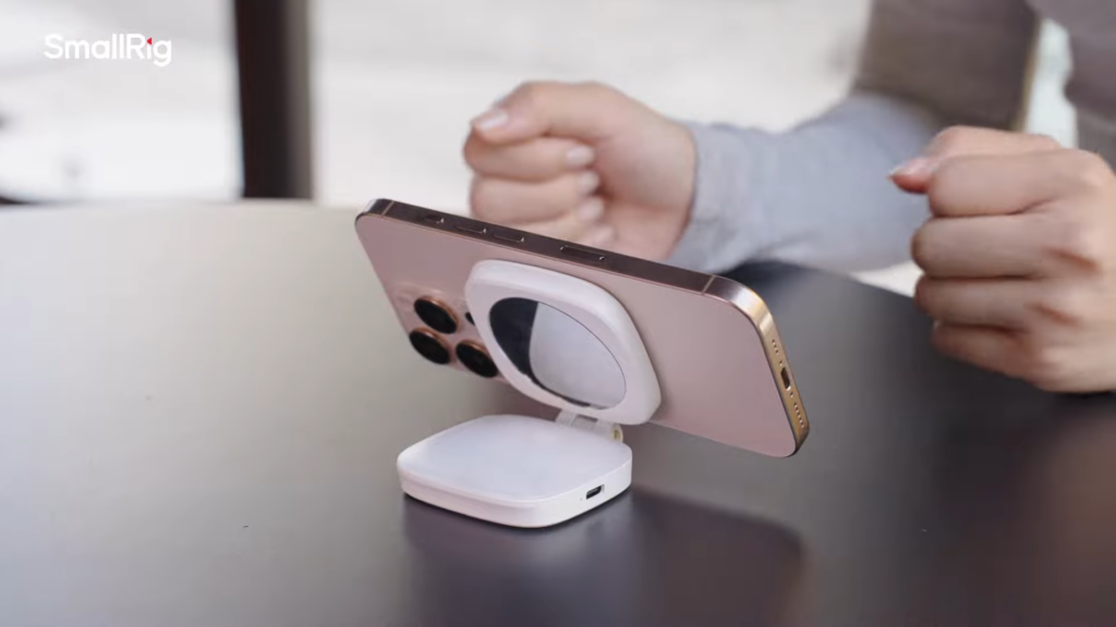 A woman using an iPhone with SmallRig Vibe P48 MagSafe Bi-Color Compact LED Light for Content Creators Mounted as a desktop stand with mirror visible