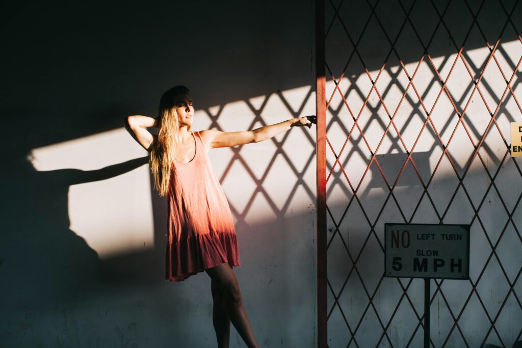 Woman posing next to a metal gate with eggcrate shadow effect using natural sunlight