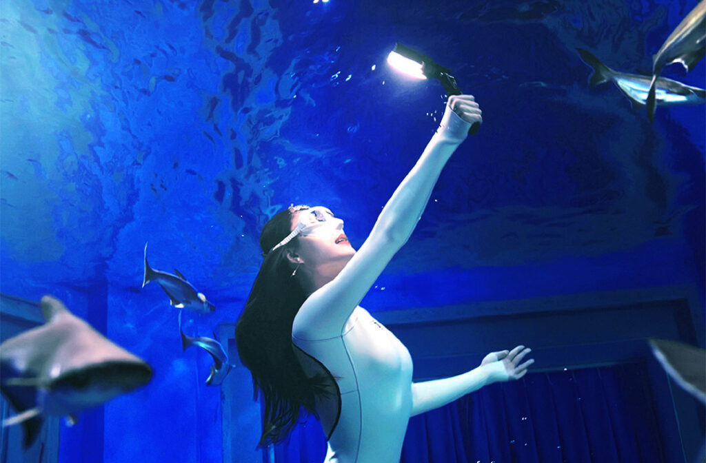 A woman recording a selfie video inside an aquarium using Godox WL8P waterproof LED light underwater