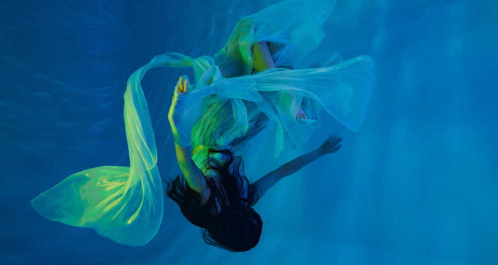 An underwater model posing floating during a photoshoot inside a pool with Godox WTR RGB tubes used