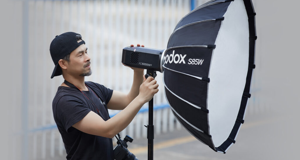 Photographer setting up the Godox AD600BMII outdoor rechargeable battery flash monohead outside with S85W softbox mounted